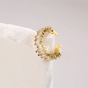 Detail of gold-plated ear cuff with baguette-cut zircons on a white textured stone