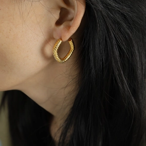 Woman wearing gold twisted hoop earrings featuring a geometric spiral textured design
