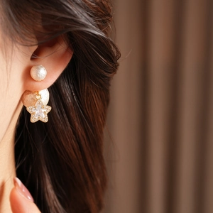 Star-shaped cotton pearl earrings with 18K gold plating worn on a model's ear