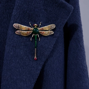 Elegant green enamel dragonfly brooch with gold metal and red gems on a navy wool coat