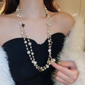 Detail of double-layer pearl necklace featuring black and white clover charms on a model