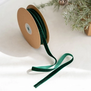 Dark green velvet ribbon on wooden spool with festive pine cones and branches