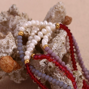 Detail of beaded necklace with freshwater pearls and red crystals on white coral