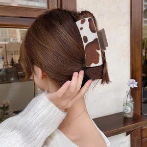 Large cow print hair claw clip worn by a model to secure a stylish bun hairstyle