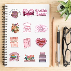 Flat lay of pink bookish stickers with floral designs on a wooden desk with a notebook