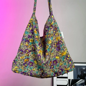 Detail of floral knit tote bag featuring purple and yellow patterns and GUAN label