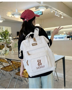 Rear view of a cream-white large capacity canvas backpack featuring a small bear embroidery