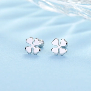 Detailed view of silver four-leaf clover stud earrings on a soft light blue fabric background
