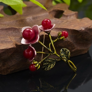 Macro detail of retro floral berry brooch with golden green leaves and red pearls
