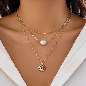 Close-up of layered gold necklace with white baroque pearl and blue gemstone pendant