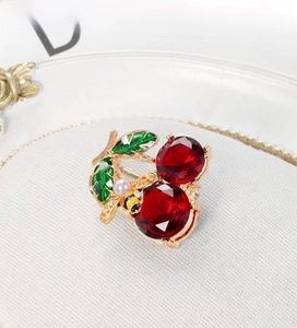 Close-up of red crystal cherry brooch with green leaf and a tiny bee detail