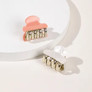Macro view of mini acrylic hair claws in pink and pearl white with gold metal teeth