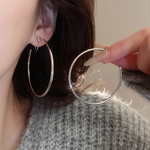 Close-up of polished silver oversized hoop earring worn against a soft grey knit sweater
