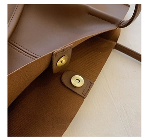 Detail view of the magnetic buckle closure on a brown leather tote bag with fine stitching
