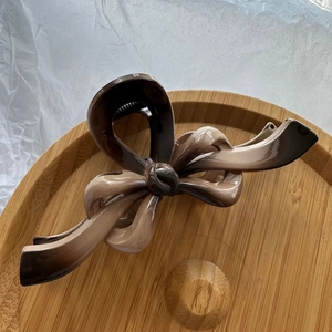 Macro detail of glossy gradient bow hair claw clip displayed on a minimalist wooden tray