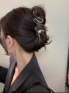 Silver wavy metal hair claw clip with pearl detail shown on a woman's hair bun