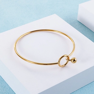 Macro detail of golden minimalist bangle featuring a solid spherical clasp on white stand