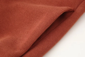 Makroaufnahme von rostrotem Strickstoff mit Ripptextur und detaillierter Seitennaht