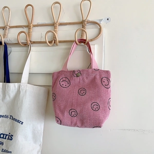 Detailed texture of pink corduroy handbag with black smiley face pattern and metal snap