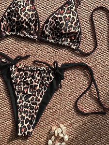 Detailed flat lay of leopard print bikini with black ties on a woven textured rug
