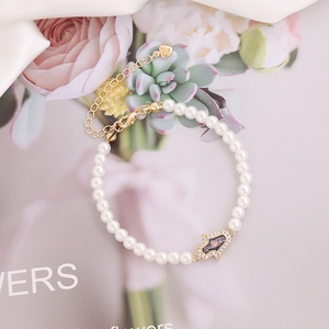 Close-up of white pearl bracelet with gold Hamsa Hand charm on white satin