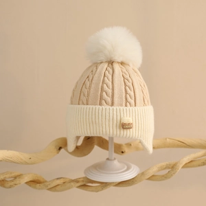 Detail of baby winter knit hat with chunky cable patterns and faux fur pom-pom