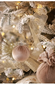 Detail of champagne velvet Christmas ornaments with gold mesh ribbon on a snowy tree