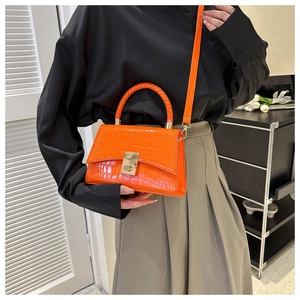 Detailed view of orange glossy crocodile pattern handbag with metal lock and woven handle