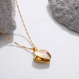 Golden heart locket necklace with pink LOVE enamel on chain against stone background