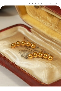 Detail of five-ball curved gold stud earrings displayed in a vintage red jewelry box