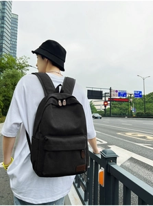 Street style shot of black canvas backpack with leather zipper and logo patch detail