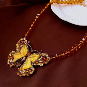 Detailed shot of amber glass bead necklace featuring a large crystal butterfly pendant