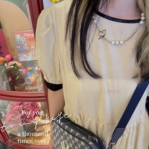 Detail of silver butterfly pendant and pearl necklace worn on a lifestyle model outfit