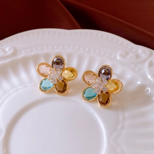 Vista macro di orecchini a fiore placcati in oro 18K con zirconi colorati su piatto ceramica