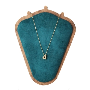 Delicate gold necklace with sparkling zircon letter A pendant on a green velvet stand