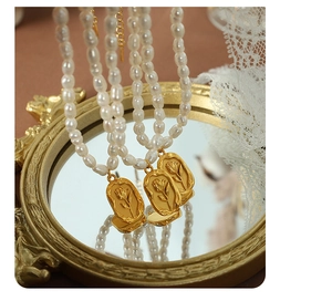 Detailed view of freshwater pearl necklace with gold rose relief pendant on vintage mirror