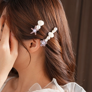 Détail de barrettes à cheveux avec strass violets, coquillages et perles sur cheveux