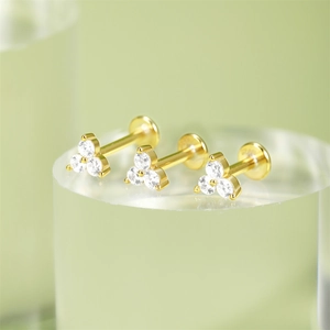 Macro shot of three gold flat back studs with clear zircons on a green background