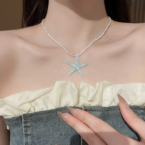 Close-up of a blue iridescent starfish pendant on a delicate white beaded necklace