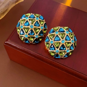 Detail of vintage round earrings with green and blue gems on a brown wooden box