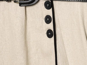 Detail eines beige Leinenkleid mit schwarzer Borte, rundem Knopf und Ledergürtel