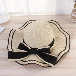 Close-up of wide brim straw sun hat featuring black ribbon bow and wavy edge trim