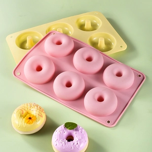 Pink and yellow 6-cavity silicone donut molds with finished donuts on a green background