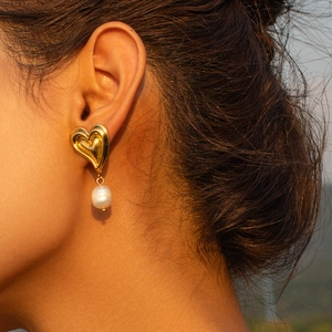 Elegant 18k gold heart stud earrings with white pearl pendants worn by a model