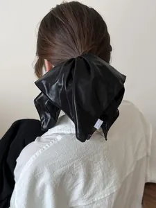 Detail of a large black satin bow hair tie with glossy finish and white side label
