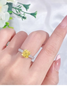 Macro shot of cushion cut yellow diamond ring on finger with white silk background