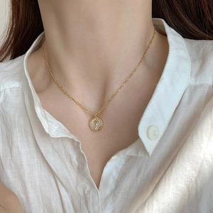 Detail of a gold flower necklace with a white mother-of-pearl pendant on a model