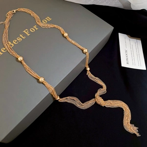 Detail of gold multilayer chain necklace with knotted tassel and bead accents on packaging