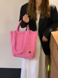 Dettaglio della borsa tote rosa in peluche con spalline lunghe indossata su un blazer nero