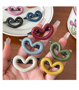 Hand holding colorful heart-shaped snap hair clips in assorted resin finishes